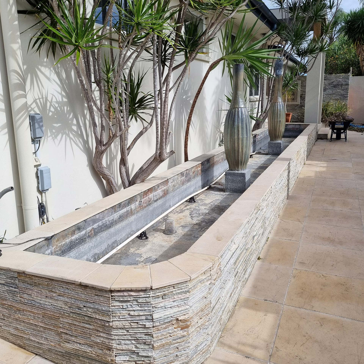 Empty outdoor water feature with stone cladding and decorative vases awaiting waterproofing restoration