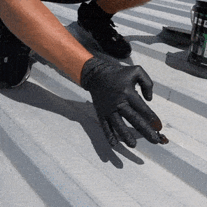 Worker using a blue sealant applicator tool to repair and waterproof a commercial flat roof surface